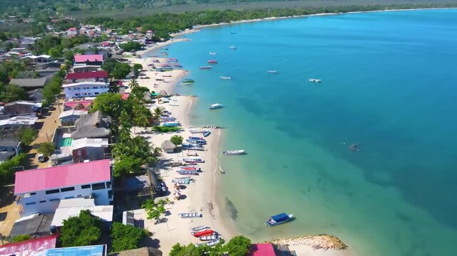 Aerial shot of turquoise Atlantic water and a sandy shoreline lined with colorful boats and red-roofed houses in Rincon del Mar, Sucre, Colombia.