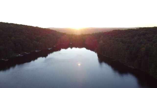 Aerial over Buckskin Lake into the sun with lens flare on a summer afternoon sunset. Lakeside cottages along side expansive wilderness of crown land located in the Tory Hill, Halliburton Highlands.