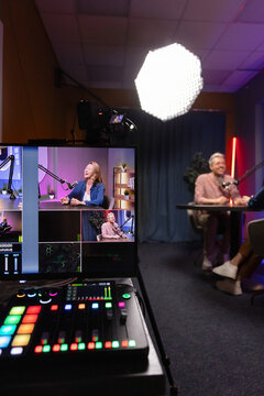 Guest and host recording podcast or talk show, engaging in digital broadcasting, audio console and monitor showing camera angles, professional studio behind scenes. Live streaming, content production