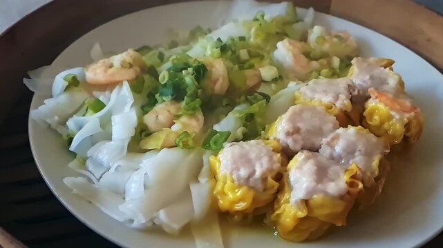 A plate of steaming hot rice noodles with prawns, spring onions, and siu mai dumplings in a bamboo steamer. 