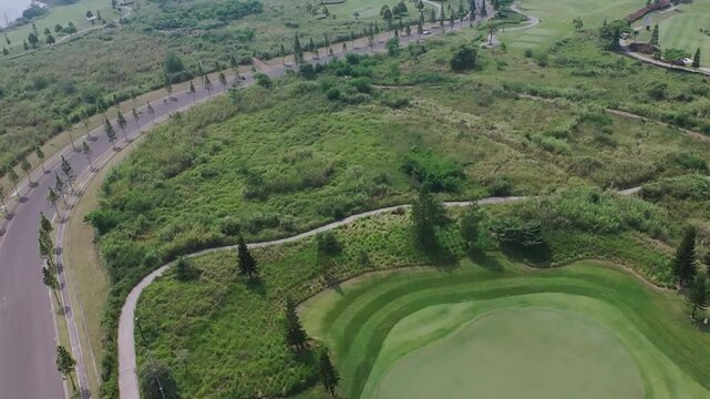Aerial View Of A Lush Green Golf Course Beside A Winding Road Sunny Day