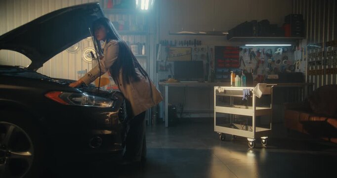 Young Female in Stylish Everyday Clothes, Having Just Arrived at Private, Well Equipped Garage. Girl By Open Hood Car, Carefully Pouring Golden Hued Maintenance Fluid Into Engine. Modern Woman.