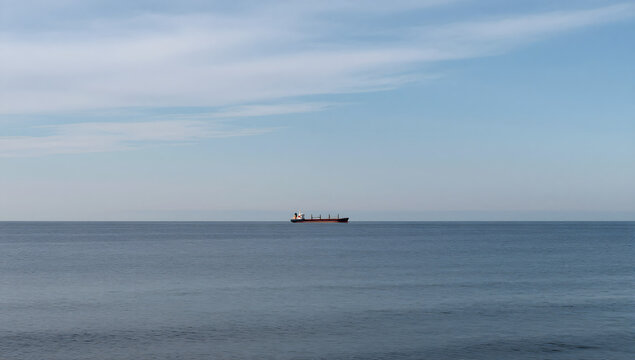 Seafaring Solitude: A solitary cargo ship cuts through the vast expanse of the open sea under a tranquil, cloud-speckled sky. 