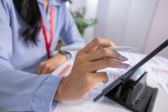 Close up of professional woman holding stylus working on digital tablet in an office focused and engaged with analytical charts document review business strategy