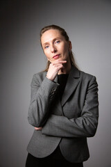 A portrait of a woman in a business suit, deep in thought, holding her chin in her hand. Vertical photo
