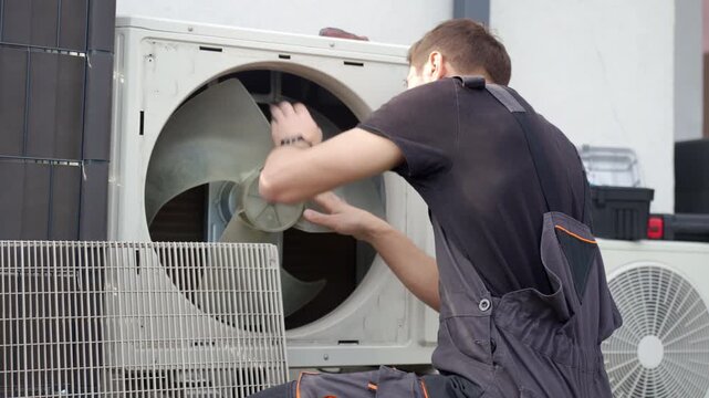 Technician removing front cover and inspecting fan inside outdoor heat pump unit. Concept of HVAC maintenance repair service and energy efficient home heating and cooling