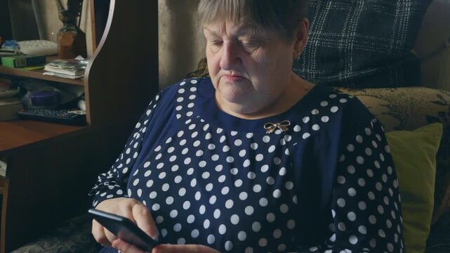 Senior woman using smartphone indoors for communication or online services. Aging population adapting to digital technology at home