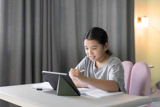 asian child smile learn from home by tablet and holding touch pen to learning drawing or writing on computer and study online class or kid girl people student fun studying on laptop by home school