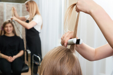 Fototapeta premium Hairstylist working on woman client with crimper