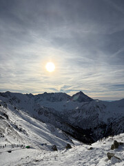 A view of the rising sun from a snow-capped mountain peak with views of other mountains and peaks © DRONAURA