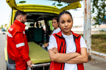 Portrait of female paramedic. Professional emergency medical team with ambulance and stretcher, healthcare and medicine concept. Serious woman first responder with arms crossed standing on street. © Graphicroyalty