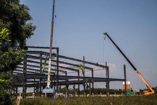 Large Steel-Frame Warehouse Structure Under Construction with Crane and Worker,Construction Workers on Cherry Picker Positioning High-Beams for New Facility
