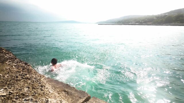 Boy Jumping from Concrete Pier into Blue Ocean, Sea. Summer Vacation Fun, Freedom, Adventure.