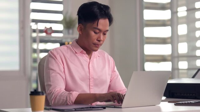 Asian young adult business colleagues review project data on tablet and laptop computer sharing ideas in bright modern office workplace