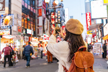 Fototapeta premium Young female tourist taking a photo of tourist and nightlife areas in Dotonbori district in Osaka, Japan