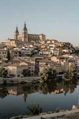 Fototapeta premium A picturesque town with a majestic cathedral and calm river at dawn exudes serene tranquility amidst warm Mediterranean architecture.