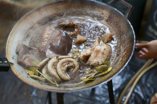 Sizzling pork offal and intestine cooking in large pan with aromatic herb. This authentic Asian street food delicacy preparation creates savory and rich traditional meal