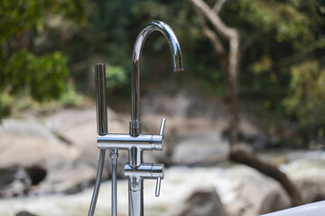 Serene, modern chrome faucet stands outdoors with beautiful, natural jungle background. luxurious and tranquil outdoor bathroom concept for spa, resort, or home © CoreRock