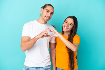 Fototapeta premium Young caucasian couple isolated on blue background making a heart with hands