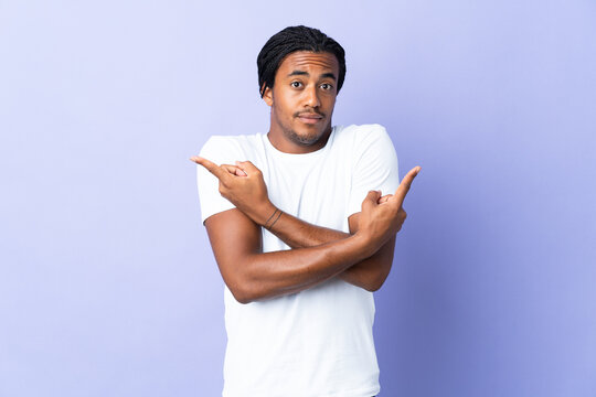 Young African American man with braids man isolated on purple background pointing to the laterals having doubts
