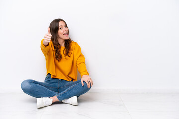 Young caucasian woman sitting on the floor isolated on white wall with thumbs up because something good has happened