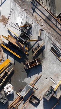 Drone shot of construction materials including formwork panels, wooden planks, and rebar scattered across a concrete slab, showing active site workflow and industrial layout.