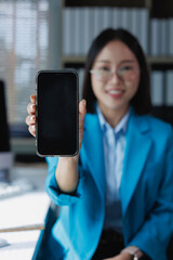 Obraz premium Smiling businesswoman in an office setting holding a modern smartphone with a blank screen, showcasing mobile technology, applications, and digital business solutions