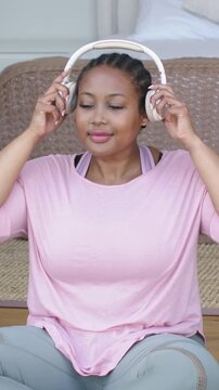 Vertical video: Lifting white headphones, woman in pink top checking fit on porch, folding in lap
