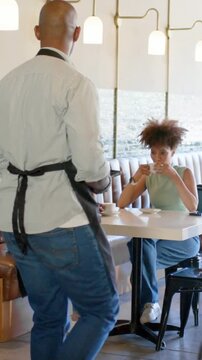 Vertical video: Talking two women in denim, green top responding to server coming with pad at cafe