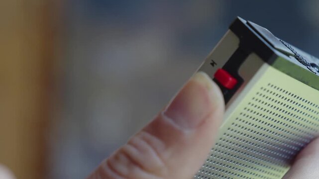 Close up of hand adjusting switch on vintage silver radio receiver with textured speaker grille and red button