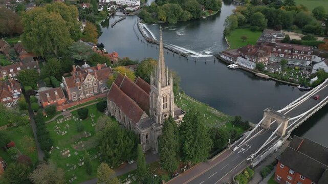 An aerial view of a church, cemetery, bridge, river with a weir, and riverside buildings.