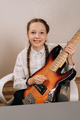 Fototapeta premium Vertical portrait of smiling preteen girl with pigtails holding bass guitar and smiling, practicing musical notes and developing a new skill, finding joy and expression in instrumental learning
