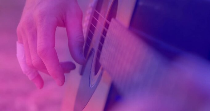 Male guitarist picking acoustic guitar for music, right hand initiating plucks, bandage, pink light