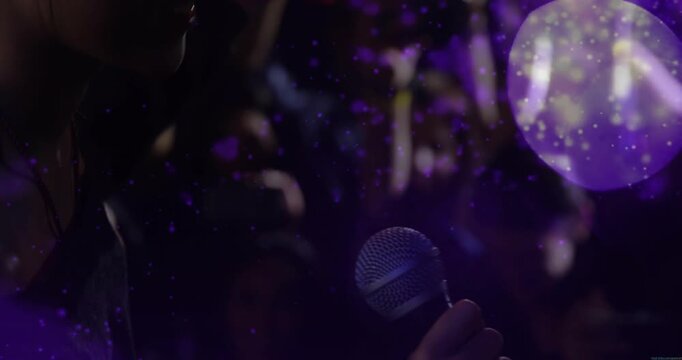 Woman singer leaning into mic as mic moving closer singing for fans with purple orbs overlaying