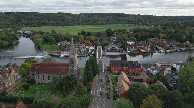 An aerial view captures a picturesque riverside town with a church, bridge, and lush greenery.