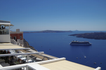 Fototapeta premium Modern cruiseship or cruise ship liner Equinox anchored in caldera of Santorini Island, Greece with harbor infrastructure and marine traffic panoramic city skyline view Mediterranean summer cruising