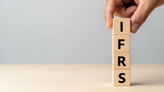 Hand stacks wooden blocks spelling out the acronym ifrs for international financial reporting standards.