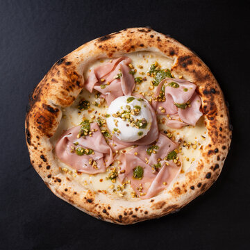 Gourmet pizza is a white pizza topped with mortadella, burrata, and pistachios. Photographed against a black background.