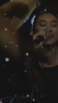 Female singer starting music, singing into mic, leaning engaging fans while sparkles overlaying