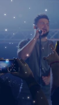 Vertical video: Music crowd phones rising to record, singer singing into mic, particles over singer