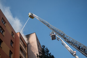 Firefighters using a turntable ladder and aerial platform to extinguish a fire in a high-rise residential building with a water jet © Tom