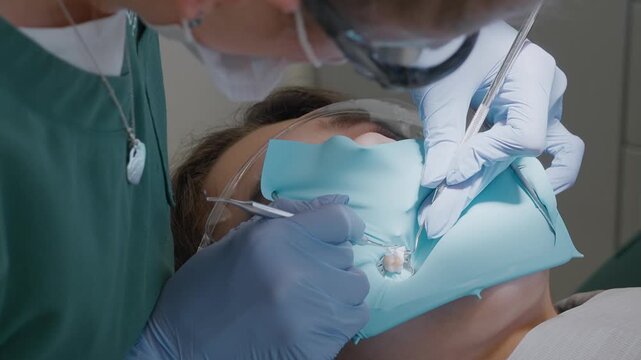 Pediatric doctor uses metal packer instrument to push gingival retraction cord into sulcus. Professional isolation technique with rubber dam to expose kid tooth margins safely.