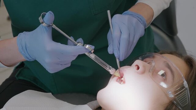 Pediatric dentist applies local anesthesia to kid upper jaw with dental syringe. Medical procedure for pain relief before tooth extraction or cavity treatment. Professional care.