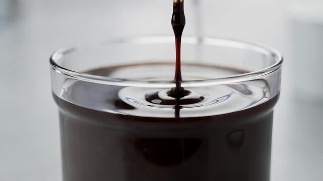 Closeup medium shot of a lowviscosity ink sample flowing slowly in a cup as the digital viscometer captures precise flow rate data highlighting smooth liquid texture.