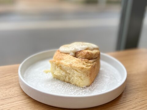 Soft and airy cinnamon roll with icing, freshly baked pastry on a wooden table, warm comfort food concept