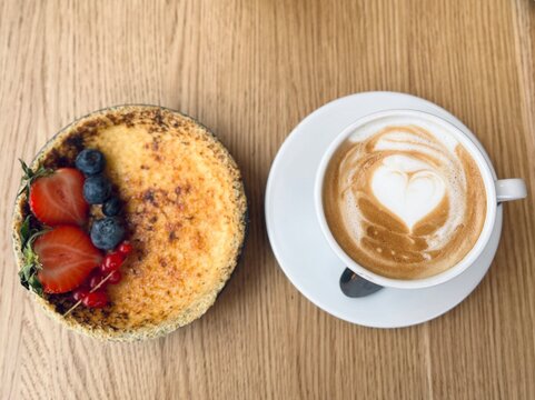 Classic French dessert cr&egrave;me br&ucirc;l&eacute;e with strawberries and blueberries, paired with coffee, soft focus background, elegant breakfast or dessert concept.