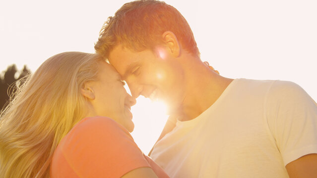 LENS FLARE: Young man and woman touching foreheads before they kiss at sunset.