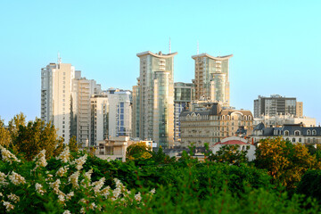 Obraz premium Modern city skyline with contemporary architecture and lush greenery in summer