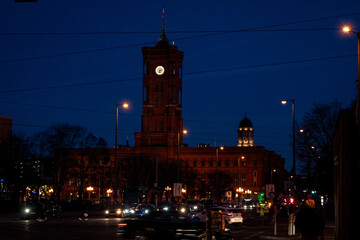 Fototapeta premium Nighttime view of a historic clock tower and surrounding architecture illuminated by warm lights against a deep blue sky.