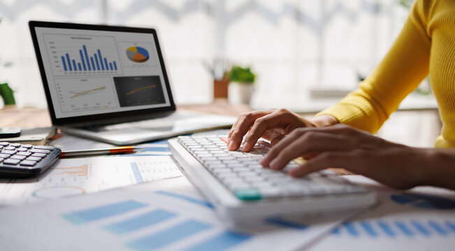 Asian business woman typing Keyboard to graphs and charts to analyze market data, balance sheet, account, net profit to plan new sales strategies to increase production capacity.